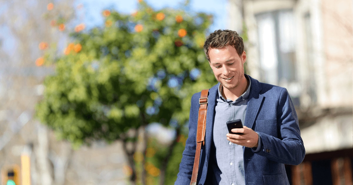 Persona caminando por la calle mientras usa su celular con una sonrisa